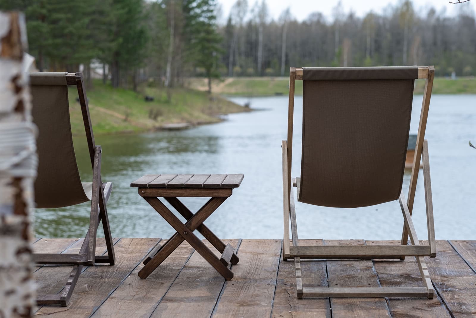 Wooden deck chairs and a table overlooking a lake