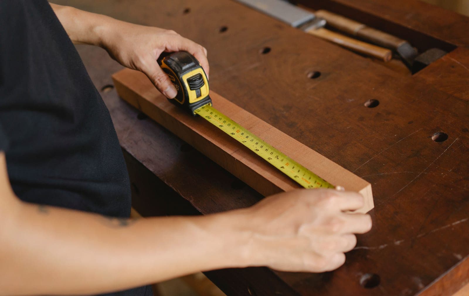 A woodworker measuring a board with a ruler on a workbench