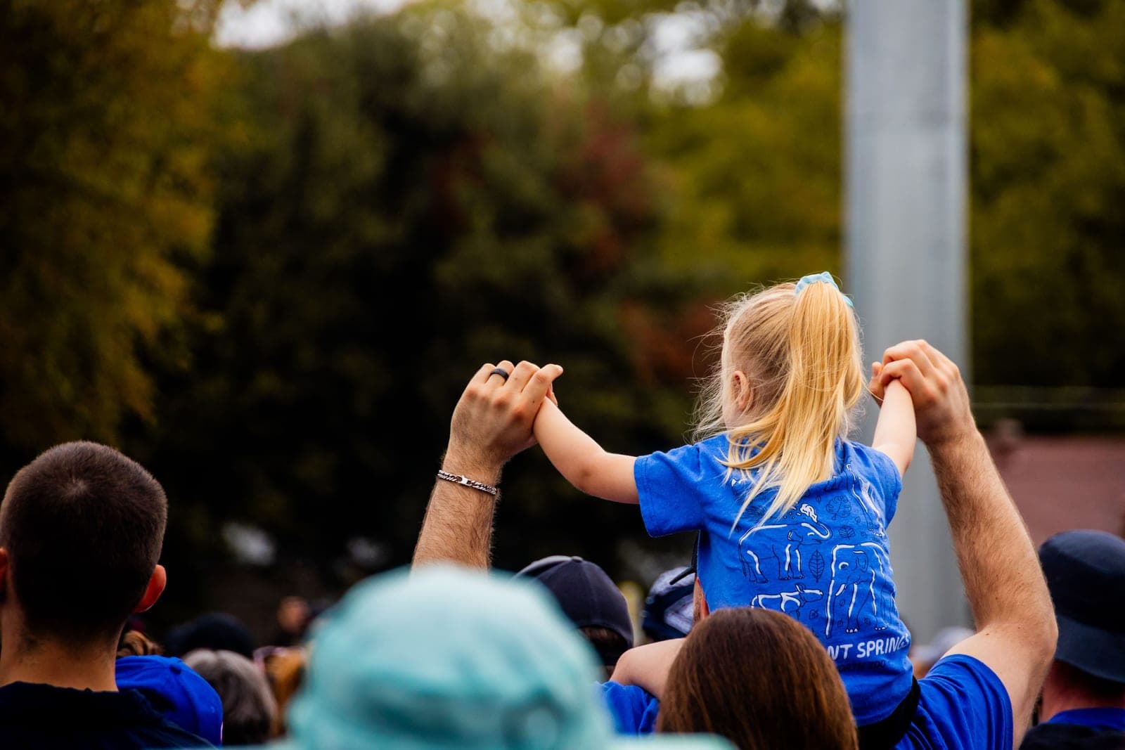 A child on a parent's shoulders in a crowd at a sunny outdoor event