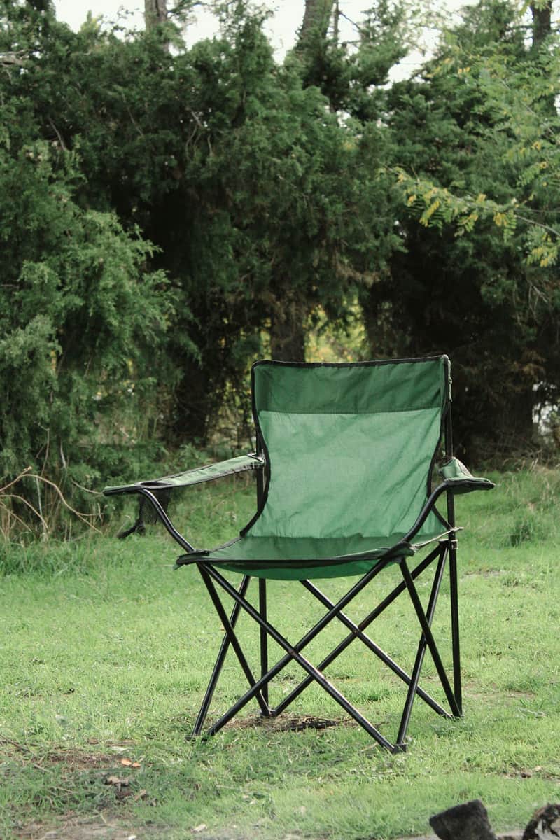 Illustrative stock photo: a green folding camp chair set outdoors against leafy trees