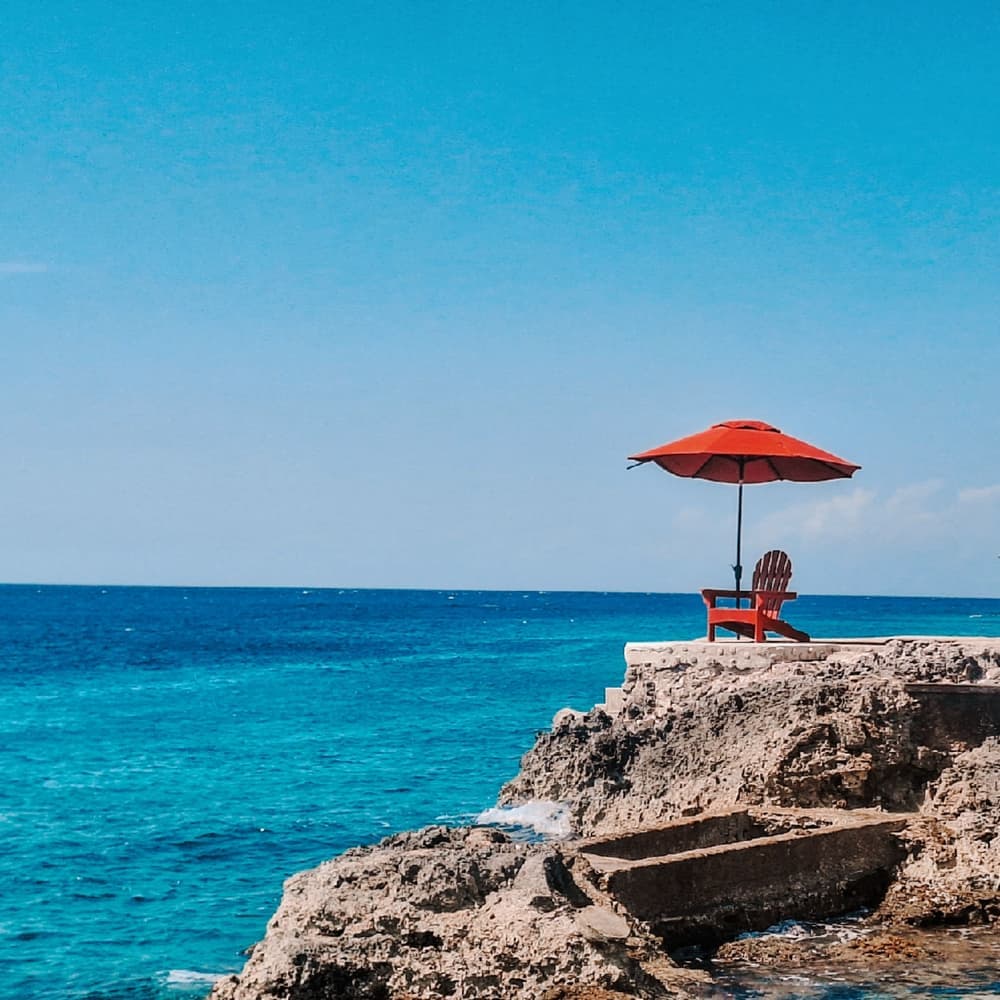Illustrative stock photo: a red chair shaded by an umbrella overlooking the sea