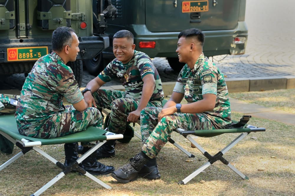 Illustrative stock photo: three people in camouflage sitting on camp cots outdoors
