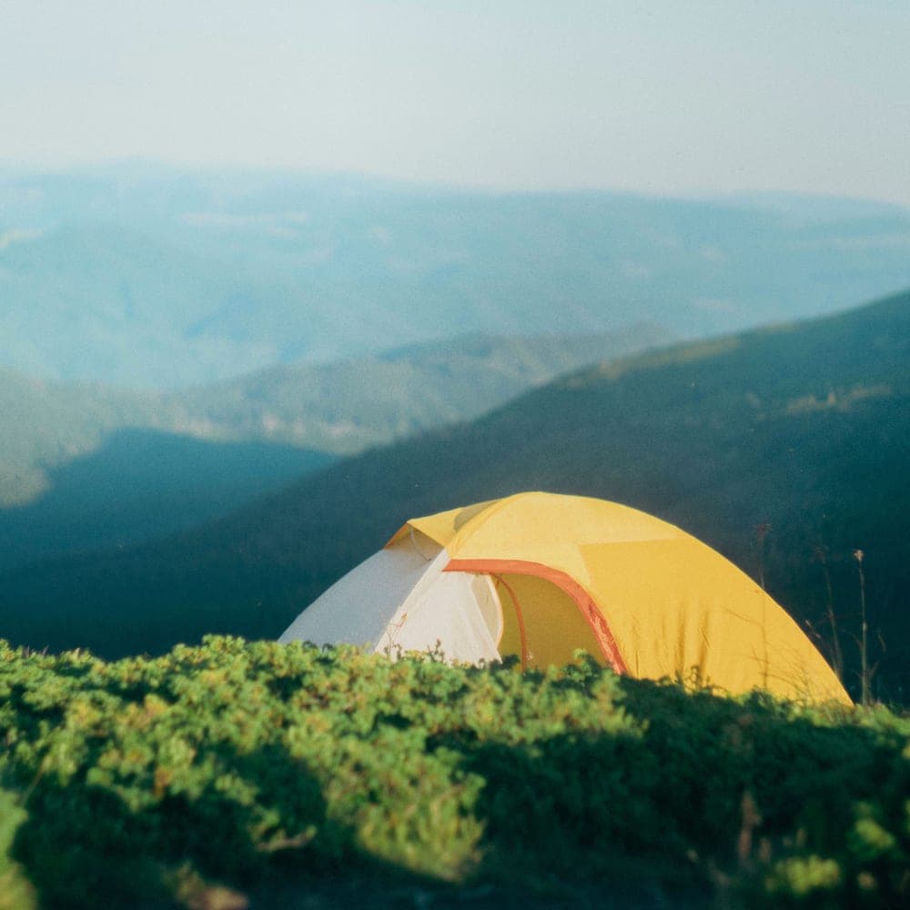 Illustrative stock photo: a tent pitched in green mountain scenery