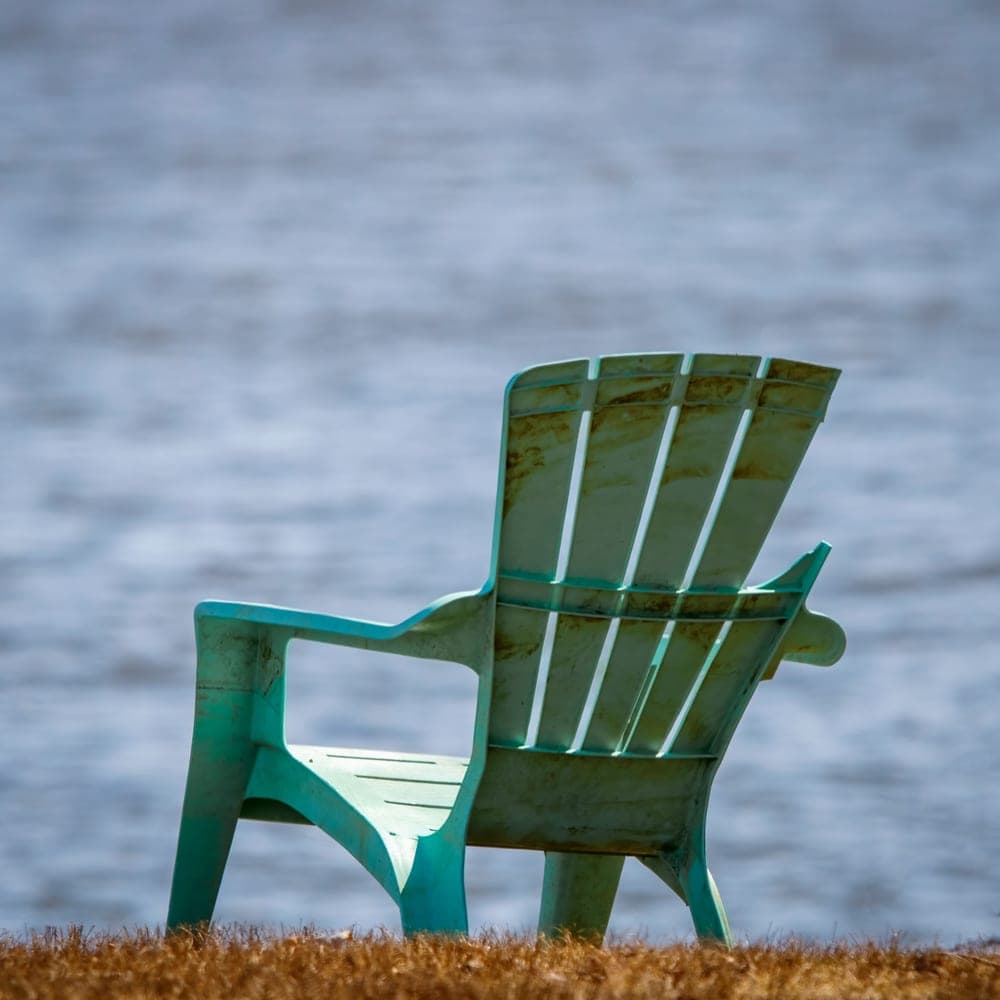 Illustrative stock photo: a turquoise Adirondack chair facing a calm lake