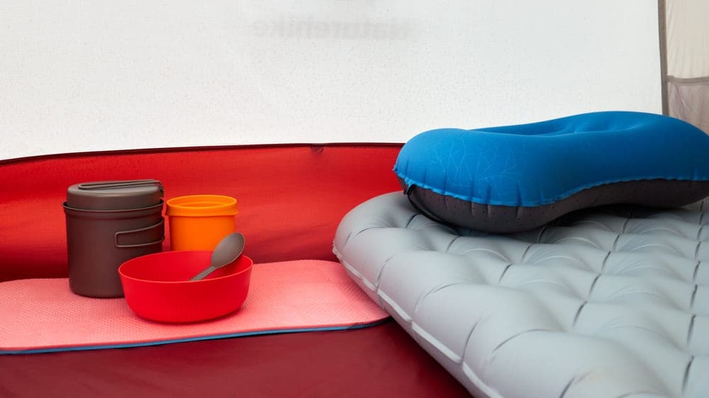 Illustrative stock photo: a sleeping pad, an inflatable pillow and cookware inside a tent