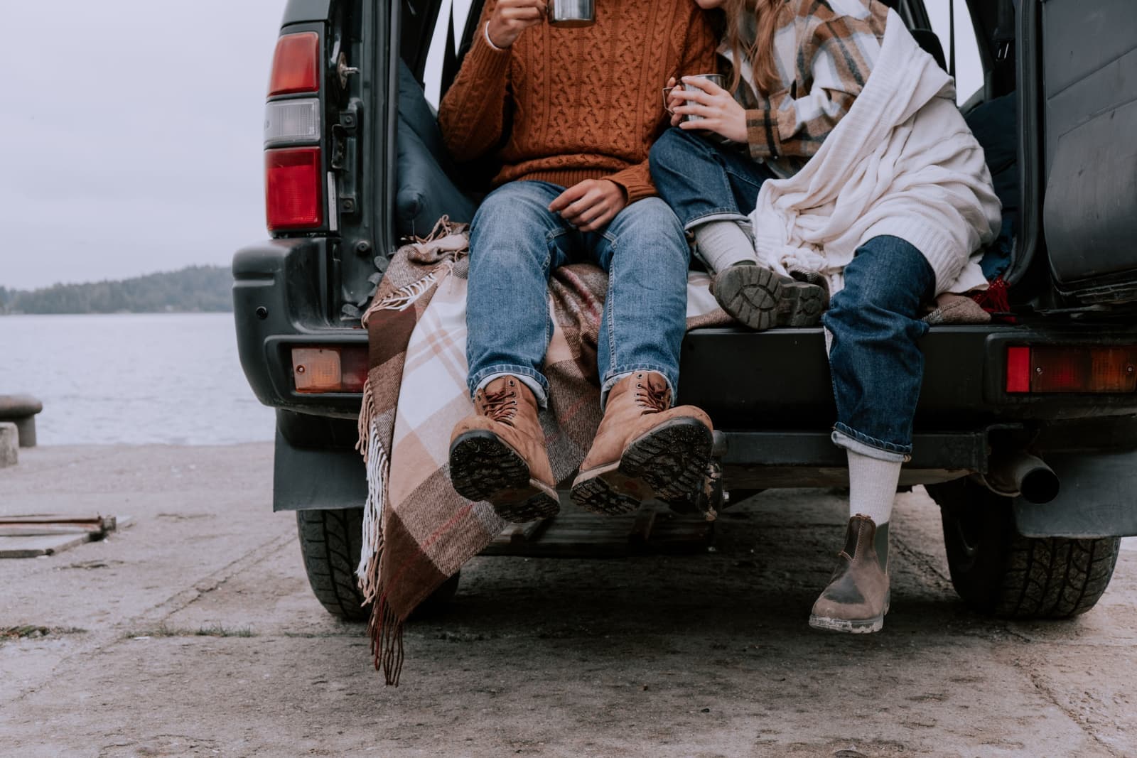 Two people sitting in the open trunk of an SUV beside a lake